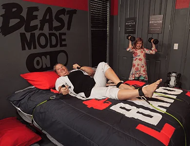 Guests posing with dumbbells on Iron Man Gym Bedroom bed with Beast Mode On sign at Lake Louisa Chateau