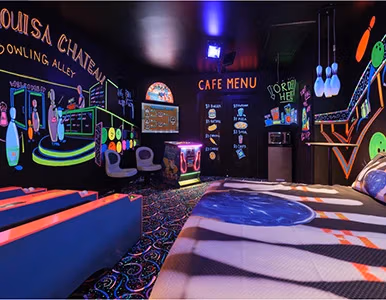 Wide view of glow-in-the-dark bowling alley room with neon murals at Lake Louisa Chateau